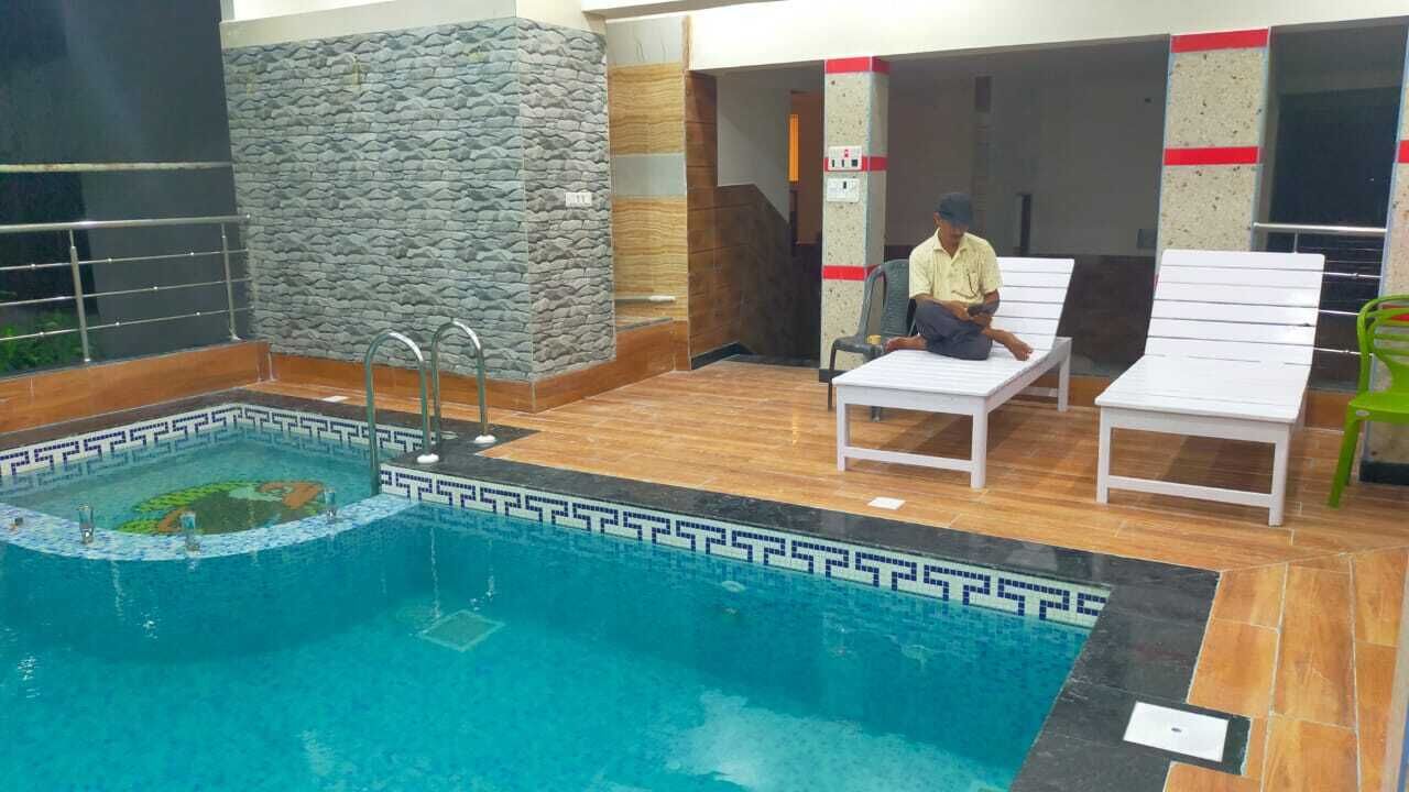 Piscina interior con pared de piedra, zona pequeña de piscina y área de descanso con una persona.