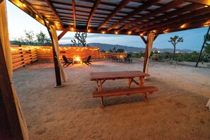 Eine Terrassensitzgelegenheit im Freien mit Holztisch und -stühlen, Lichterketten und Blick auf die Wüstenlandschaft.