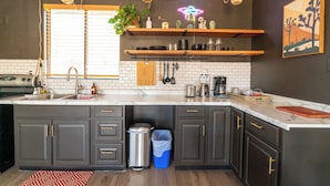 A modern kitchen with dark cabinets, white countertops, and a neon sign above the sink. - Cozy casita on quiet desert hillside with views, fire pit and grill! (Yucca Valley)