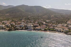 A coastal town with buildings along the beachfront, a boat on the water, and mountains in the background.
