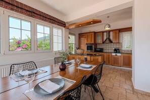 Una cocina moderna con armarios de madera, una mesa de comedor para dos personas y grandes ventanales con vistas a un jardín.