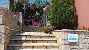 Un escalier en pierre mène à une villa appelée Villa Artia, qui est entourée d’une végétation luxuriante et de plantes en fleurs.
