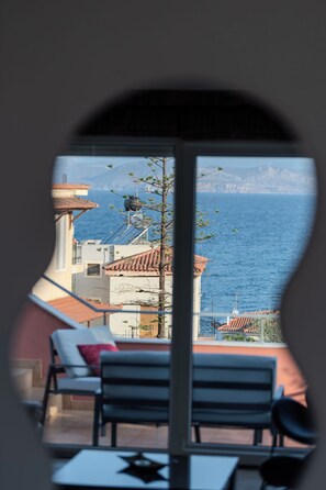 A room with a view of the sea, a balcony, and a table with a chair.
