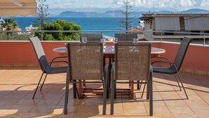 Une terrasse avec une table et des chaises, offrant une vue sur la côte et les montagnes au loin.