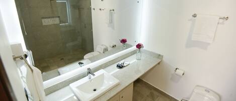 Un baño moderno con un espejo grande, un lavamanos, un inodoro y una zona de ducha.