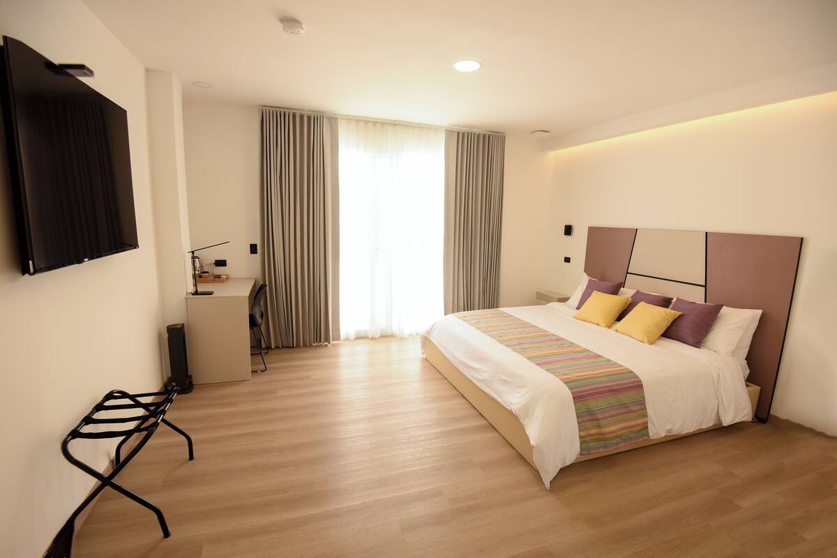 A modern hotel room with a large bed, a desk, and a TV mounted on the wall.