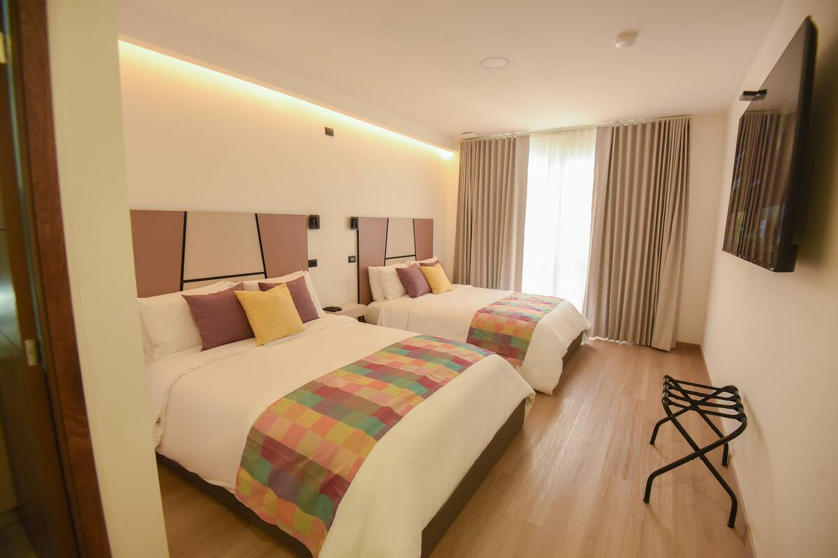 A hotel room with two beds, a TV, and a wooden floor.