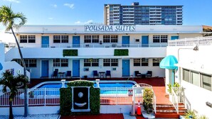A hotel named Pousada Suites with a pool area, outdoor seating, and a view of a tall building in the background.
