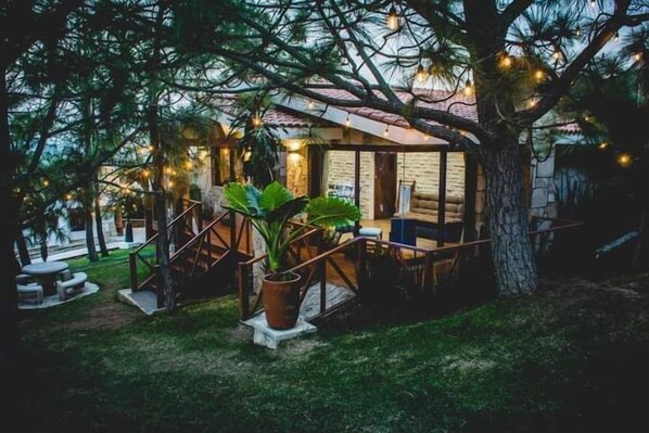A cozy outdoor seating area with a wooden deck, surrounded by trees and potted plants.