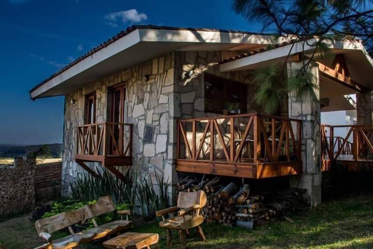 A stone house with a balcony, wooden furniture, and a stack of firewood.