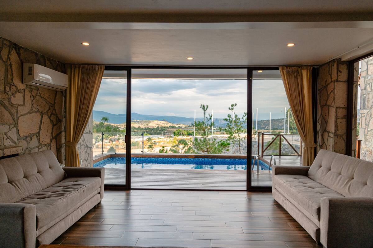 A spacious room with a large sliding glass door leading to a pool area, two sofas, and stone walls.