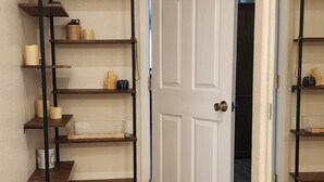 Un pasillo con suelo de madera, una puerta blanca y una estantería metálica decorada.