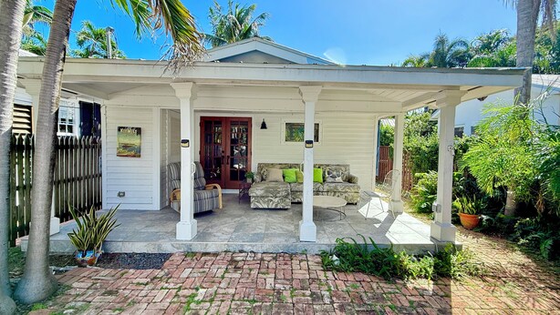 A covered porch with a white railing, a wooden door, and a stone bench. - Beautiful Old Town 2 bedroom Cottage on a Private Lane (Key West)