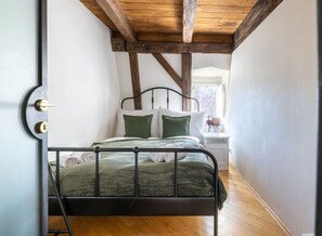 A bedroom with a metal bed frame, a wooden ceiling, and a white nightstand with a lamp.