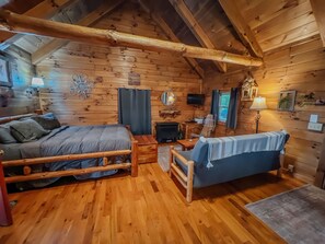 A cozy log cabin interior with a bed, a sofa, a chair, a fireplace, and a television.