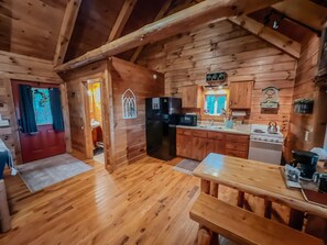 A wooden cabin interior with a kitchen, dining area, and a red door.