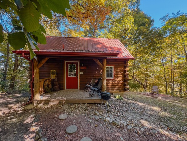 A rustic cabin with a red door, wooden porch, and a small outdoor seating area.