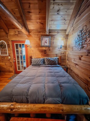A wooden cabin room with a bed, a door, and a wall-mounted picture.