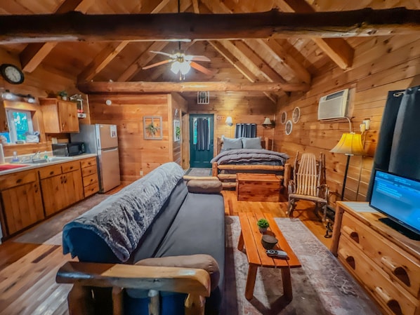 Ein rustikales Blockhaus-Interieur mit einer Couch, einem Holztisch, einem Fernseher und einer Küchenzeile.