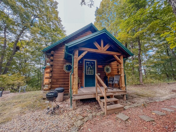 A rustic cabin with a wooden porch, a door, and a small set of stairs leading up to it. - Maple Lane Cabin in Hocking Hills (Laurelville)