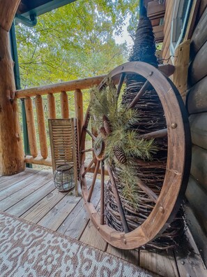 A wooden wheel with pine branches and pinecones, a lantern, and a wooden bench on a wooden deck.