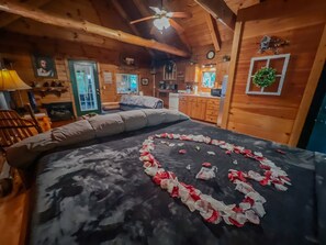 A cozy cabin room with a bed adorned with rose petals, wooden walls, and a rustic ceiling.