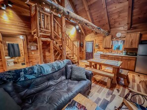 Ein gemütliches Blockhaus-Interieur mit Sofa, Esstisch, Küchenbereich und einer Treppe.