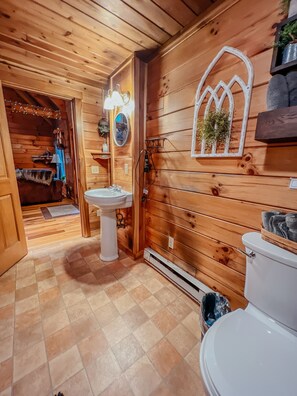 Baño de cabaña de madera con lavabo blanco, inodoro y espejo con marco decorativo.