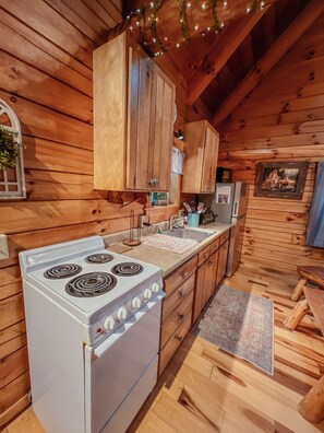 Cocina de cabaña de madera con estufa blanca, armarios de madera y un lavamanos pequeño.