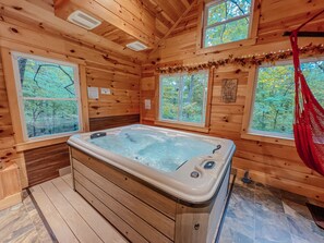 Una cabaña de madera con jacuzzi, ventanas amplias y una hamaca.