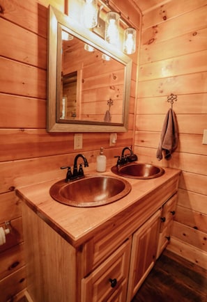 Un baño tipo cabaña de madera con dos lavabos, un espejo y una toalla colgada en la pared.