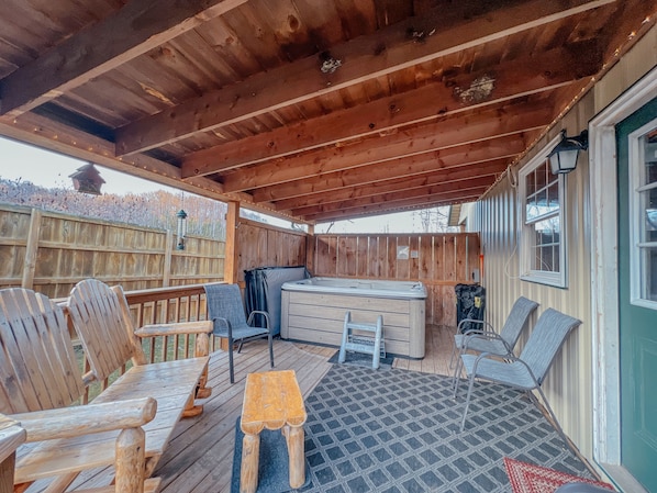 A covered patio with wooden furniture, a hot tub, and a view of a wooden fence.