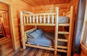 A wooden bunk bed room with a ladder, a small table, and a window with curtains.