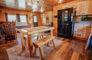 L’intérieur d’un chalet en bois comprend une table à manger, un banc et un coin cuisine équipé d’un réfrigérateur.
