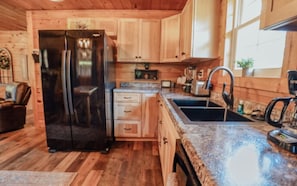 A compact kitchen with wooden cabinets, a black refrigerator, a granite countertop, and a sink.