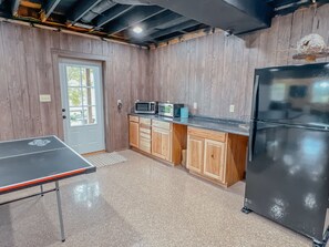 A kitchen with wooden cabinets, a black refrigerator, a microwave, a toaster, and a ping pong table. - Ash Ridge Lodge in Hocking Hills (Laurelville)