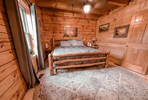 A wooden cabin bedroom with a bed, nightstand, and a large window.