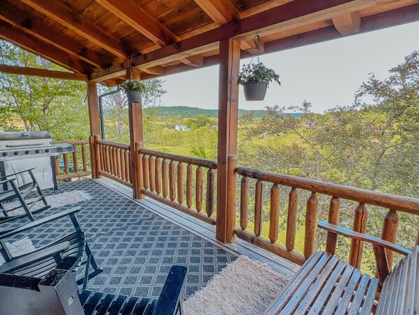 A covered outdoor area with a barbecue grill, seating, and hanging planters. - Ash Ridge Lodge in Hocking Hills (Laurelville)