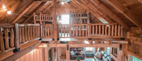 Een ruime loft-stijl cabin met een hoge plafond, houten balken, een zithoek met een bank en stoelen, en een keuken met houten kastjes en een aanrecht.