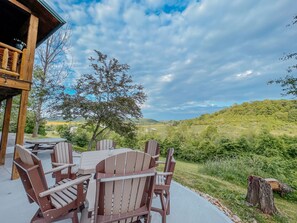A wooden deck with Adirondack chairs and a table, overlooking a lush green landscape and hills. - Ash Ridge Lodge in Hocking Hills (Laurelville)