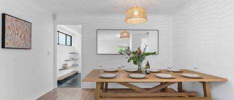 Un comedor con una mesa de madera dispuesta para cuatro personas, una lámpara colgante y un espejo en la pared.