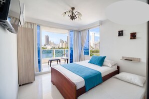 A modern hotel room with a large bed, a balcony with a view of the city, and a ceiling fan. - Apartamento AL1-LM Cerca al mar con Aire (Cartagena)