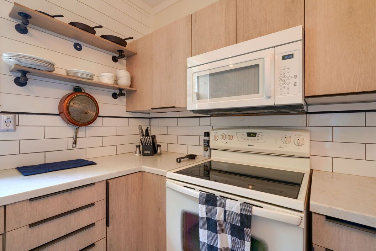 A kitchen with white cabinets, a microwave, an oven, and a hanging pot strainer.