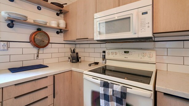 A kitchen with white cabinets, a microwave, an oven, and a hanging pot strainer.