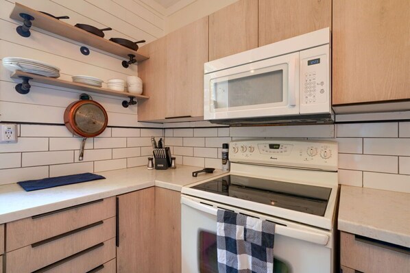 A kitchen with white cabinets, a microwave, an oven, and a hanging pot strainer.