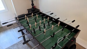 Una mesa de futbolín en una habitación con una lámpara y una ventana.