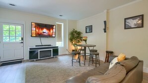 A living room with a leather sofa, a TV mounted on the wall, a dining table with chairs, and a plant.
