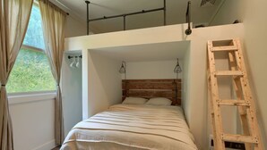 Un dormitorio con una cama nido, una escalera de madera y una ventana con cortinas.