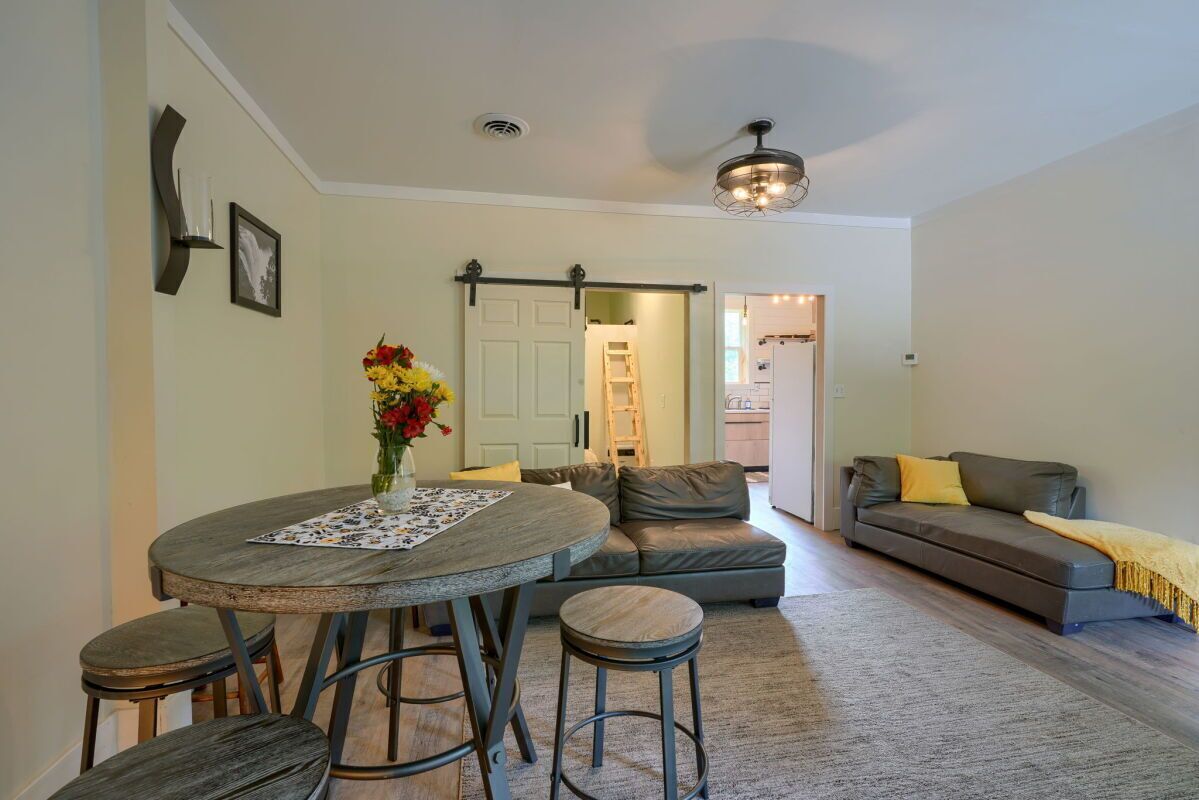 A dining area with a round table, stools, and a vase of flowers. There is a sofa and a couch in the background.