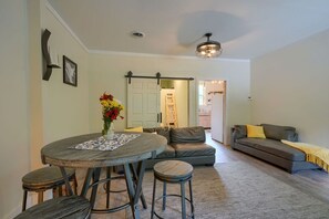 A dining area with a round table, stools, and a vase of flowers. There is a sofa and a couch in the background.